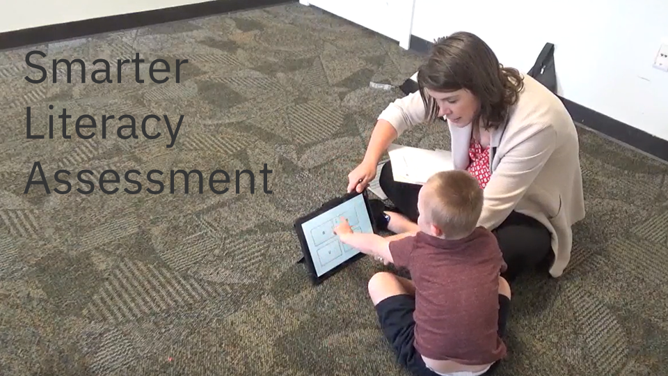 Adult assessing a child's literacy while sitting on the floor. The text "Smarter Literacy Assessment" is overlayed.
